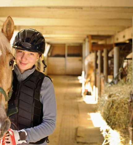 Young female rider with horse inside stable Young female rider with horse inside stable