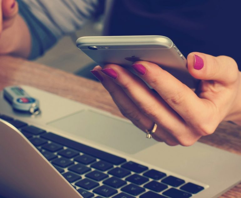 lady on laptop with mobile phone in her hand