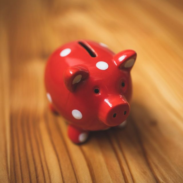 Image of a red ceramic piggy bank on a wooden desk.